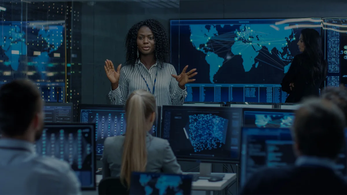 Equipe em uma sala de monitoramento com telões exibindo mapa-múndi e painéis de dados.